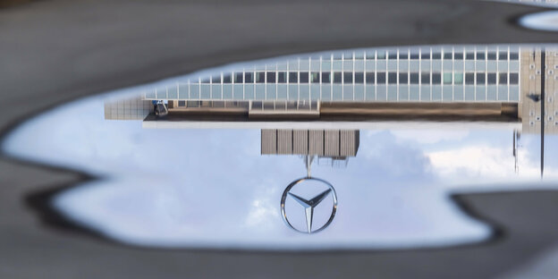 Ein Mercedesstern auf dem Gebäude der Konzernzentrale spiegelt sich in einer Wasserpfütze