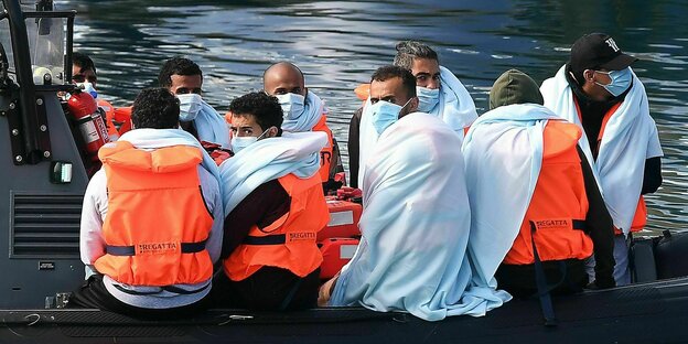 Migranten mit oangen Rettungswesten und Mundschutz auf einem Rettugsboot