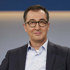 Cem Özdemir trägt eine Brille und Anzug und schaut lächelnd in die Kamera