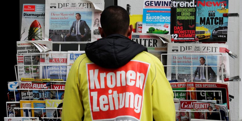 Ein Mann mit einem Logo der Kronen zeitung steht vor einem Zeitungsstand