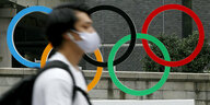 Ein Mann mit Gesichtsmaske voir den Olympischen Ringen