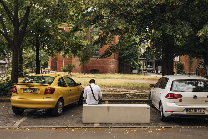 Mann sitzt auf einem Betonblock zwischen zwei parkenden Autos