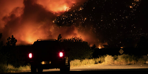Ein Auto steht Nachts vor einem Wildfeuer