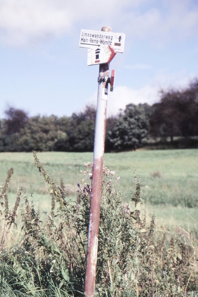 Ein Wegzeichen in der Landschaft, es zeigt einen schwarzen Turm auf weißem Hintergrund