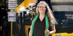 Frau mit grauen Haaren steht vor einem Berliner Bus an einer Haltestelle