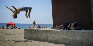 Ein Junge macht einen Salto Rückwerts. Im Hintergrund der Strand