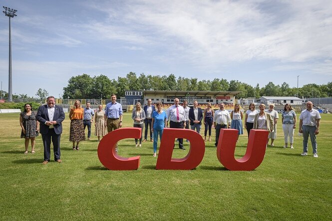 Menschen versammeln sich auf einem Sportplatz hinter dem Logo der CDU