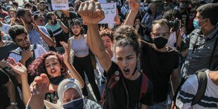 Junge Frauen und Männer halten die Arme und Transparente bei einer Demonstration hoch.