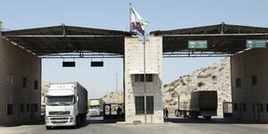 Der Grenzübergang Bab al Hawa in Syrien. Er besteht aus zwei Durchfahrten, die durch eine Mauer voneinander getrennt sind. Die Durchfahrten haben kleine Dächer. Ein LKW fährt gerade in die eine, ein anderer in die andere Richtung hindurch.