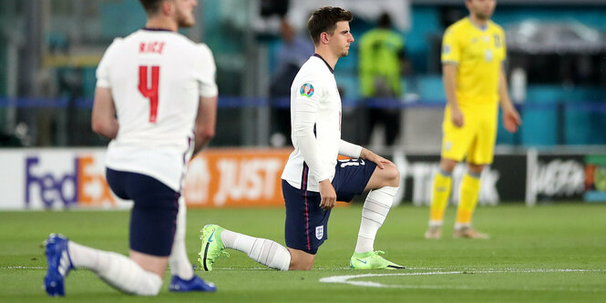 Zwei englische Spieler knien vor dem Spiel auf dem Rasen nieder.