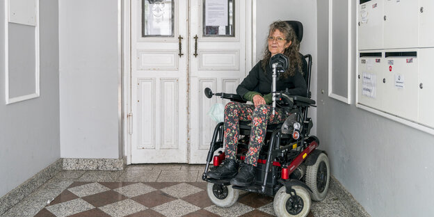 Frau sitzt im Rollstuhl neben einer weißen Eingangstür