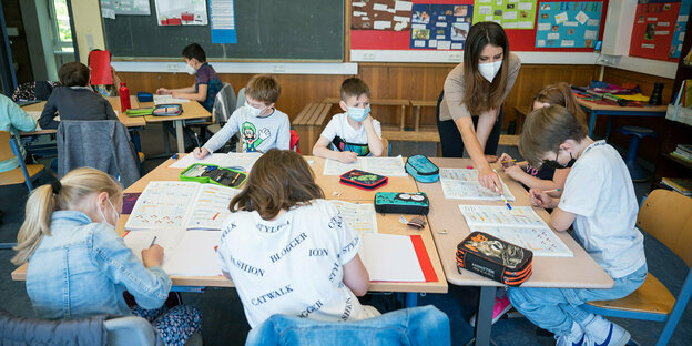 SchuelerInnen mit Maske um einen Tisch im Klassenraum
