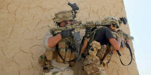 Zwei Soldaten mit Maschinengewehren im Anschlag gehen ninter einer Mauer in Deckung
