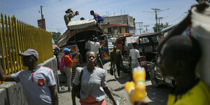 Straßenszene aus Port-au-Prince - Menschen auf einem Markt , im Hintergrund verladen zwei Männer eine Matzratze auf das Dach eines Minibusses