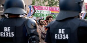 Im Vordergrund zwei Polizisten in schwarzer Montur, zwischen ihnen Demonstranten mit einem Plakat "Queers for a free Palestine"