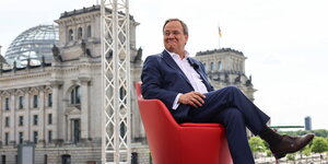 Armin Laschet sitzt in einem roten Sessel - im Hintergrund das Reichstagsgebäude