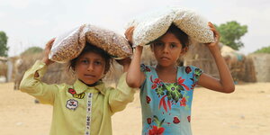 Zwei Mädchen tragen Nahrungsmittel in Plastikverpackung auf dem Kopf