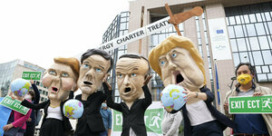 Klimaaktivisten mit riesigen Köpfen, die Ursula von der Leyen, Mark Rutte, Emmanuel Macron und Angela Merkel darstellen, demonstrieren vor dem Gebäude des Europäischen Rates in Brüssel