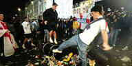 Ein englischer Fan kickt mit seinem Fuss eine Mülltonne weg, umringt von anderen Fans