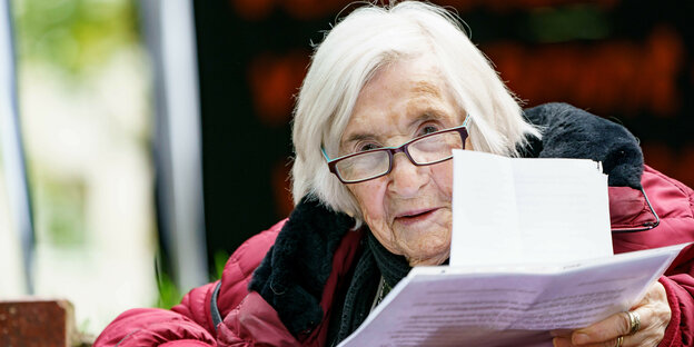 weißhaarige, alte Frau mit Papierbögen in der Hand