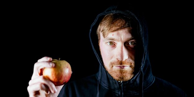 Karl Bär Agrarwissenschaftler schaut in die Kamera, hält einen Apfel in der Hand und trägt eine Kapuze auf dem Kopf