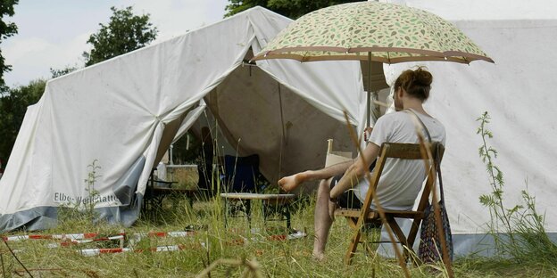 Ein junger Mann sitzt auf einer Wiese vor einem Zelt