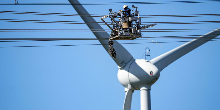 Bau einer neuen Leitungstrasse - Ein Monteur arbeitet an einer Höchstspannungsletiung , im Hintergrund weine Windkraftanlage