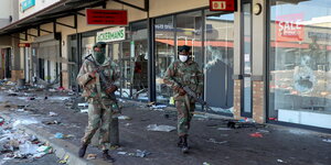 Zwei Soldaten laufen bewaffnet mit Maschinengewehren vor geplünderten Geschäften entlang