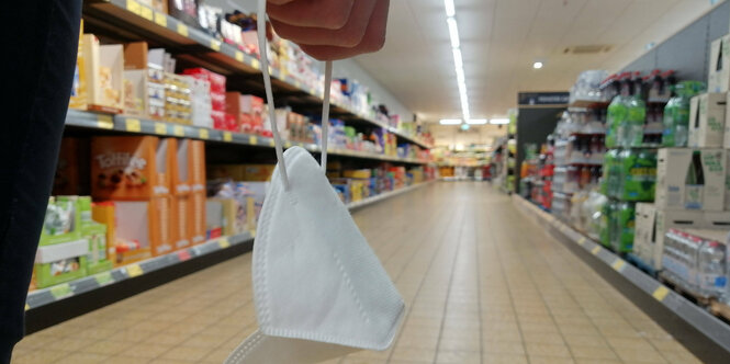 Eine Frau im Supermarkt trägt eine FFP2 Maske in der Hand