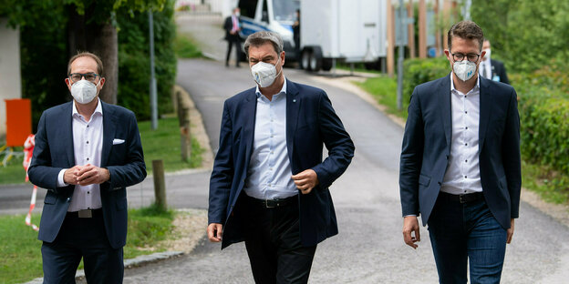 Alexander Dobrindt, Markus Söder und Markus Blume tragen Mund-Nasenschutz und laufen eine Straße entlang