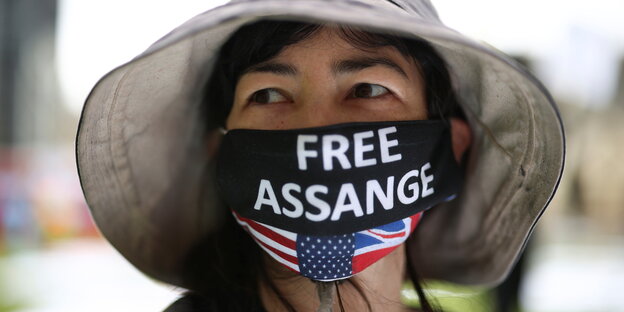 Frau mit Hut trägt eine Gesichtsmaske: Free Assange
