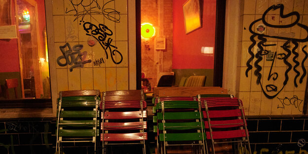 Vier zusammengestellte Stuhlreien stehen vor einer erleuchteten Bar in Neukölln