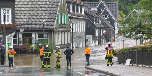 Feuerwehrleute stehen vor einer überschwemmten Straße Feuerwehrleute stehen vor einer überschwemmten Straße