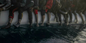 Beine von Flüchtlingen hängen von einem Rettungsboot