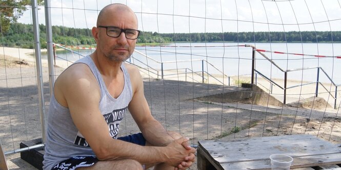 Bar-Betreiber Marco Benz sitzt vor dem Zaun, der den Helenesee absperrt.