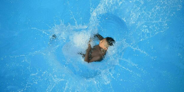 Ein Kind springt in einen Pool und das Wasser spritzt hoch