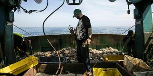 Fischer steht auf Boot mit Krabbe in der Hand