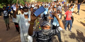 Demonstranten auf der Straße in Khartum halten die Hände hoch.