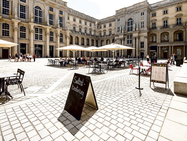 Einer von zwei Innenhöfen des rekonstuierten Stadtschlosses: man sieht den gepflasterten Innenhof mit einem Café mit Tischen und Stühlen und Schirmen Einer von zwei Innenhöfen des rekonstuierten Stadtschlosses: man sieht den gepflasterten Innenhof mit einem Café mit Tischen und Stühlen und Schirmen