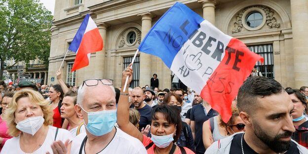 Menschen, mit und ohne Mase, protestieren. Auf einer französischen Fahne steht: "Freiheit!"