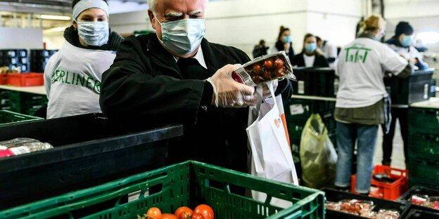 In einer großen Halle packen ehrenamtliche Helfer mit Masken Lebensmittel in Tüten