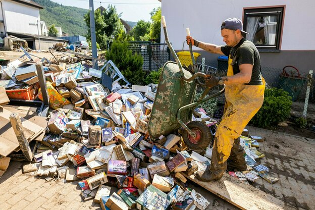 Ein Mann räumt mit der Schubkarre zerstörte Bücher in Ahrbrück beiseite