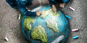 Zwei Kinder malen mit Kreide aufwändig einen Globus auf dem Asphalt