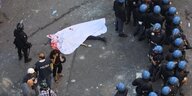 Eine mit einem Tuch bedeckte Leiche liegt auf eine Straße neben Polizisten.