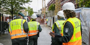 Zollbeamte mit Helmen auf einer Baustelle.