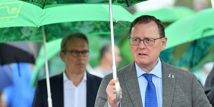 Ein Mann im Anzug unter einem grünen Regenschirm. im hintergrund: zahlreiche weitere Regenschirm