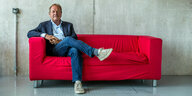 Frank Bsirske sitzt auf rotem Sofa.