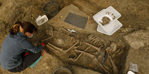 Eine Frau legt ein Skelett in einem Grab frei.