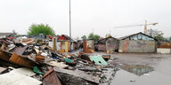 Hinter einer Müllhalde stehen provisorisch zusammengebaute Behausungen.