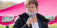 Eine Frau steht vor einem rosa Regenschirm und spricht in ein Mikrofon
